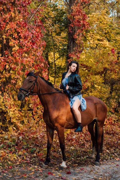 Hermosa joven se sienta a horcajadas sobre un caballo con un vestido y botas y mira hacia el lado