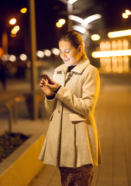 Hermosa joven con smartphone en la calle por la noche