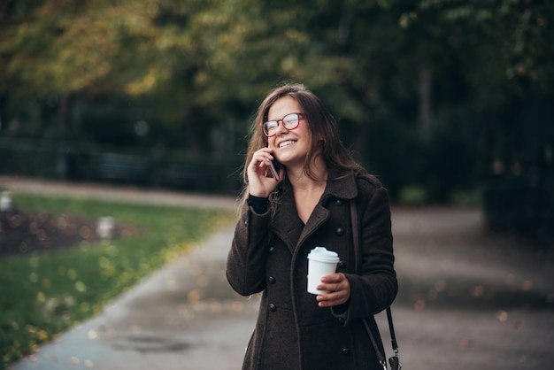 Hermosa joven con smartphone y tomando café para llevar