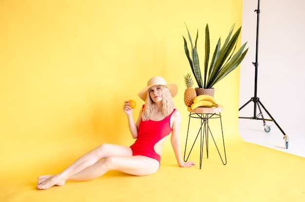 Foto una hermosa joven con sombrero de paja sentada cerca de un fondo amarillo concepto de comida sana