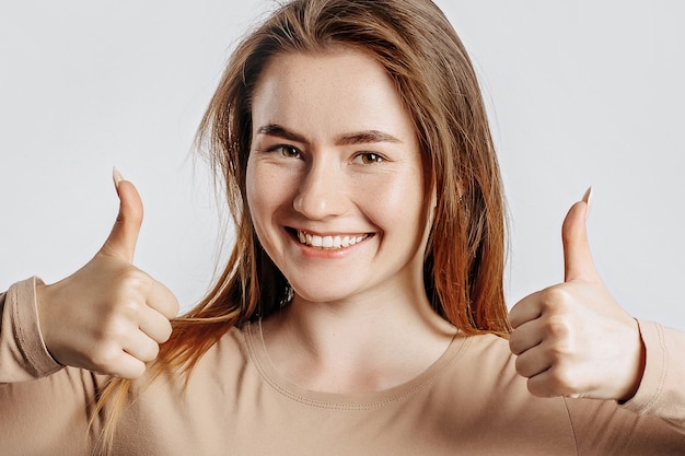 Foto hermosa joven sonriendo y muestra los pulgares para arriba gesto con las dos manos sobre un fondo blanco aislado.