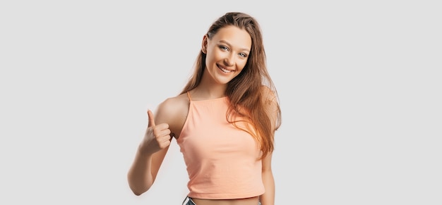 Hermosa joven sonriendo y muestra los pulgares para arriba gesto de la mano sobre un fondo blanco aislado. Mujer positiva apunta a una idea, un lugar para la publicidad.