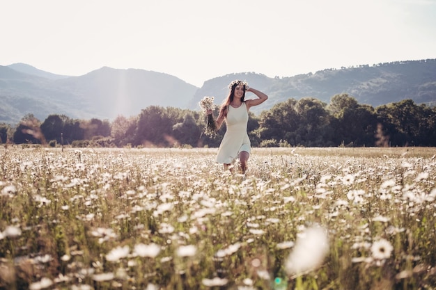 Hermosa joven sonriendo sobre el campo de manzanilla Mujer morena feliz y despreocupada con cabello largo saludable divirtiéndose al aire libre en la naturaleza