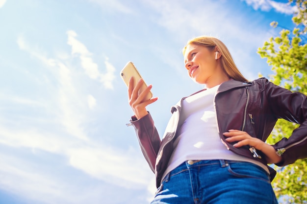 Hermosa joven sonriente adulta caucásica niña caminando al aire libre en el parque con comunicación por chat con auriculares inalámbricos