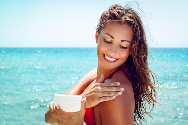 Hermosa joven sonriente aplicando bronceador en la playa.