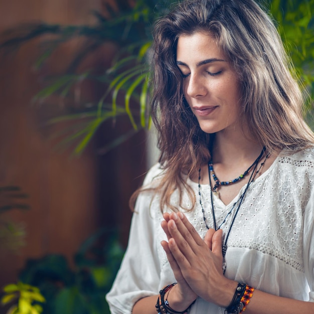 Hermosa joven sonriente y consciente parada con los ojos cerrados y las manos en posición de oración o gesto de Namaste