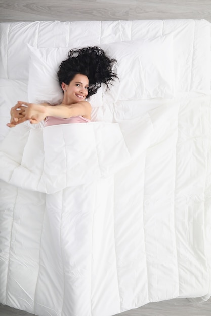 Hermosa joven sonriente se encuentra en una cama grande con lino pastel blanco