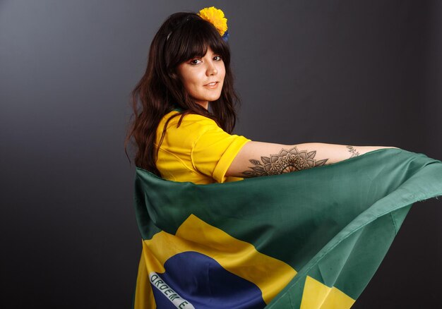 Hermosa joven sonriente feliz sosteniendo la bandera de Brasil con camiseta de fútbol