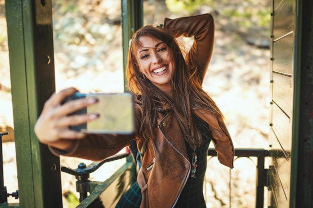 Una hermosa joven sonriente se hace selfie en un tren retro y viaja en una aventura.