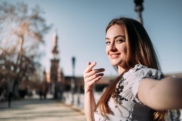 Hermosa joven sonriente mostrando su viaje por España e invitando a seguirla