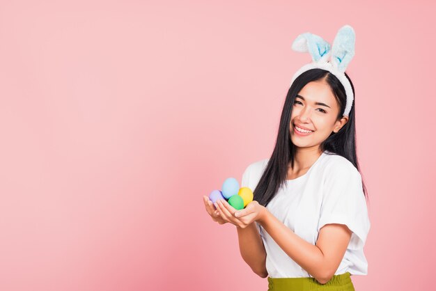 Hermosa joven sonriente con orejas de conejo sosteniendo coloridos huevos de Pascua regalo en las manos