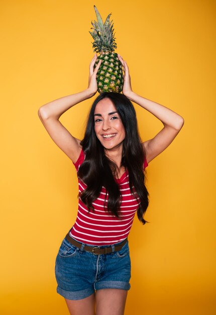 Hermosa joven sonriente con piña en las manos sobre fondo naranja Frutas tropicales Alimentación saludable