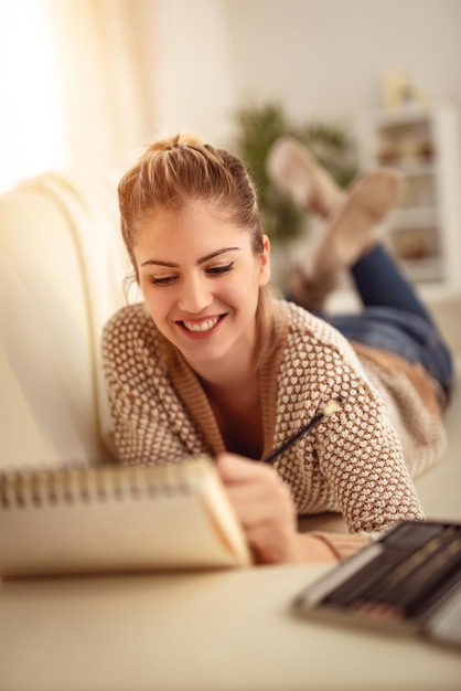 Hermosa joven sonriente relajándose dibujando en un cuaderno de bocetos con lápices de colores en casa.