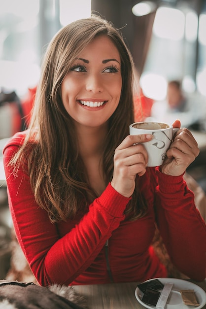 Foto hermosa joven sonriente relajándose y disfrutando de una taza de café en la cafetería.