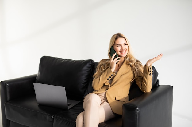 Hermosa joven sonriente relajándose en un sofá en casa usando un teléfono móvil