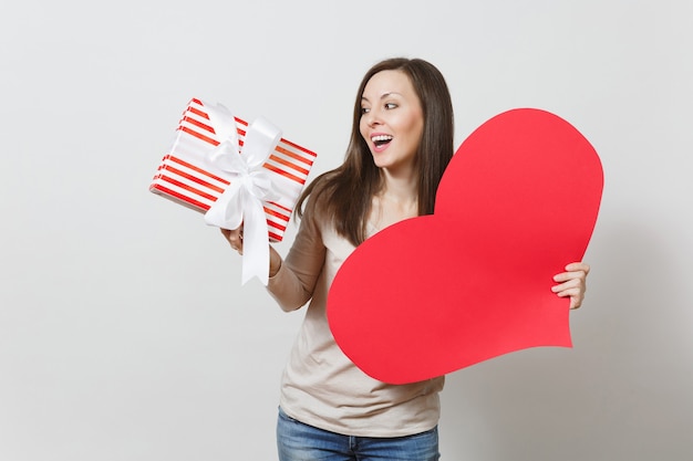 Hermosa joven sonriente sosteniendo un gran corazón rojo, caja con presente sobre fondo blanco. Copie el espacio para publicidad. Con lugar para texto. Concepto de día de San Valentín o día internacional de la mujer.