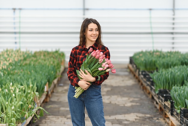 Hermosa joven sonriente, trabajador con flores en invernadero. tulipanes, caja con flores. Copie el espacio.