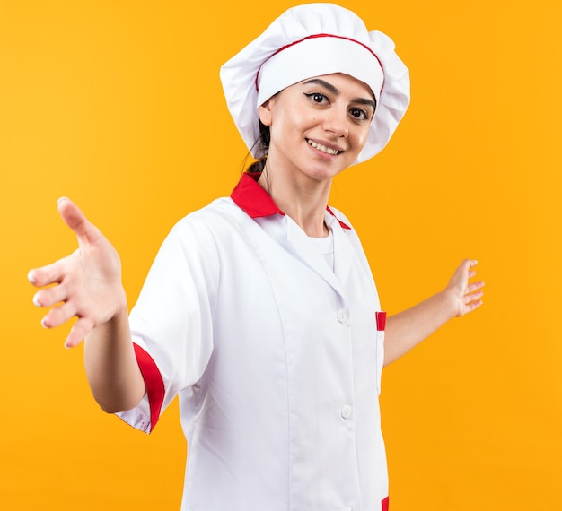 Hermosa joven sonriente en uniforme de chef extendiendo las manos