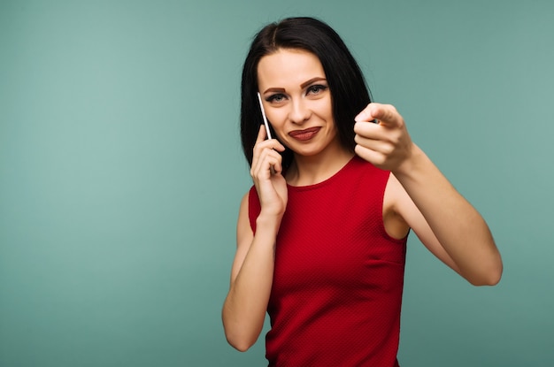 Foto hermosa joven sorprendida caucásica hablando por su teléfono celular apuntando a la cámara de fondo aislado - imagen