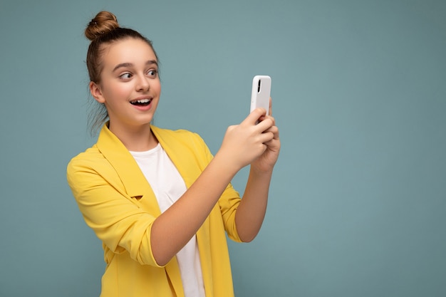 Hermosa joven sorprendida vestida con chaqueta amarilla y camiseta blanca que se encuentran aisladas sobre azul