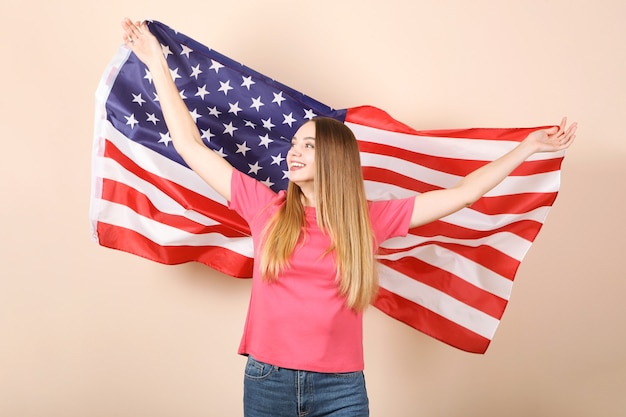 Hermosa joven sosteniendo la bandera de Estados Unidos sobre un fondo de color