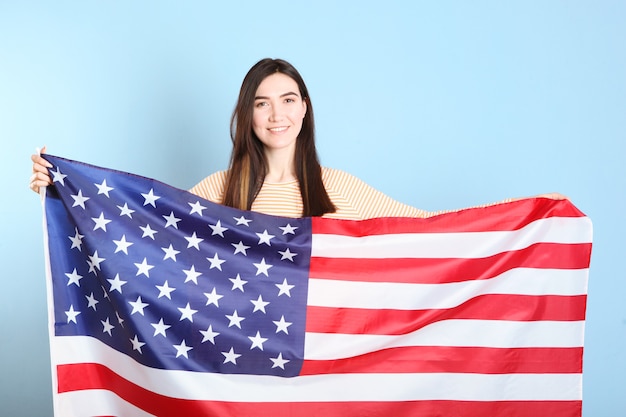 Hermosa joven sosteniendo la bandera de Estados Unidos sobre un fondo de color