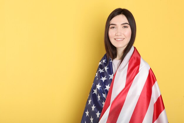 Hermosa joven sosteniendo la bandera de Estados Unidos sobre un fondo de color