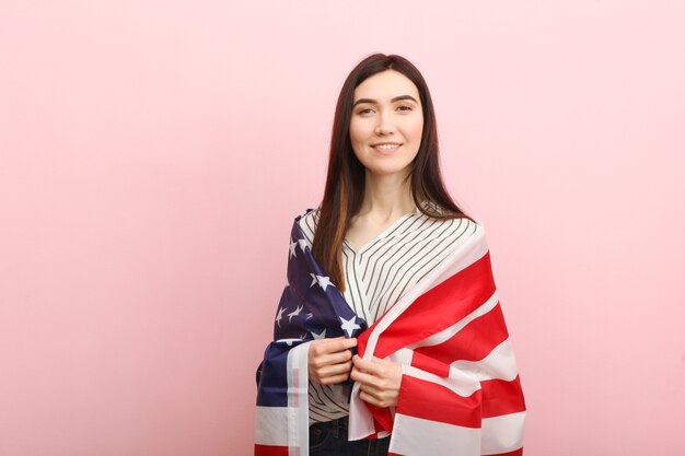 Hermosa joven sosteniendo la bandera de Estados Unidos sobre un fondo de color