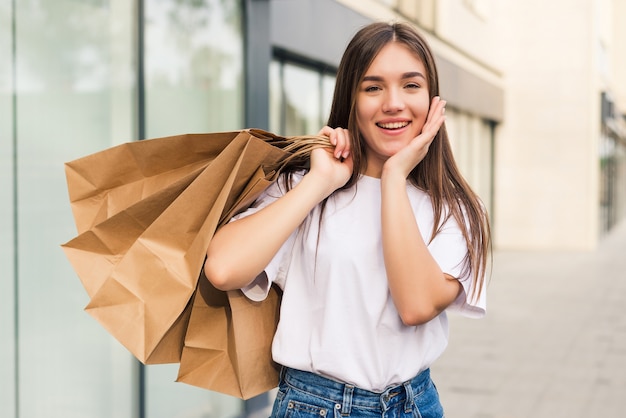 Hermosa joven sosteniendo bolsas de la compra y sonriendo al aire libre