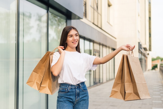 Hermosa joven sosteniendo bolsas de la compra y sonriendo al aire libre