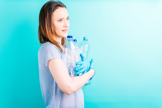 Hermosa joven sosteniendo botellas de plástico sobre fondo azul. concepto de reciclaje. cuidado del medio ambiente