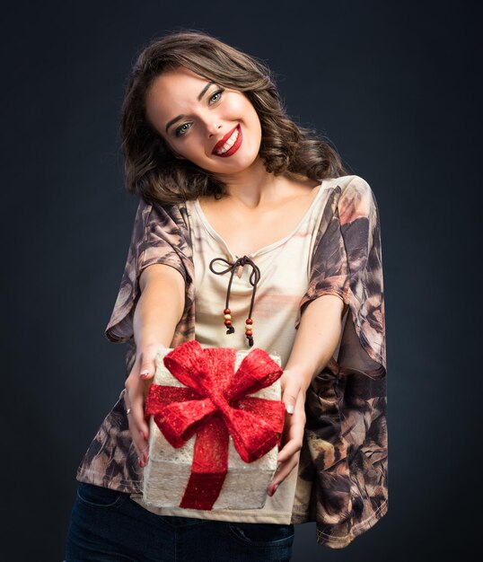 Hermosa joven sosteniendo una caja de regalo en un fondo oscuro