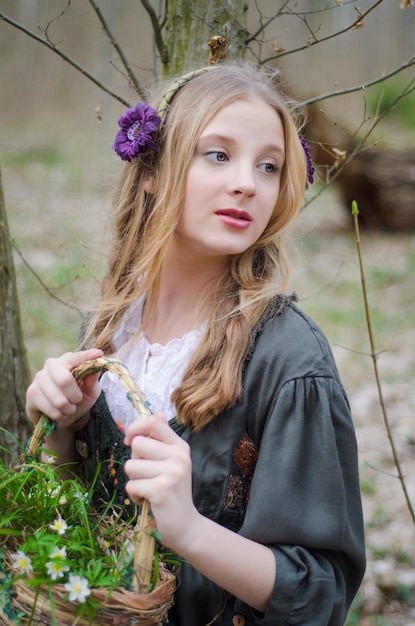 Hermosa joven sosteniendo una canasta de flores silvestres y mirando hacia otro lado