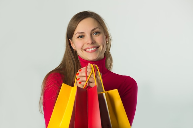 Hermosa joven sosteniendo una compra en bolsas blandas sobre una pared blanca