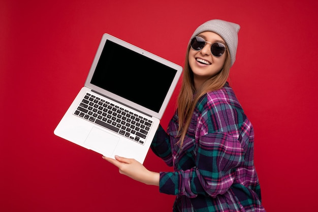 Hermosa joven sosteniendo la computadora portátil mirando a la cámara aislada