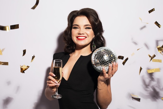 Hermosa joven sosteniendo una copa de champán y una bola disko