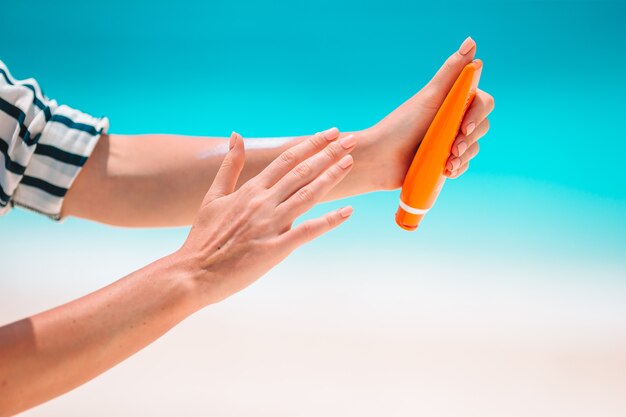 Hermosa joven sosteniendo una crema solar tumbado en la playa tropical