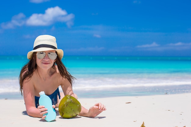 Hermosa joven sosteniendo una crema solar tumbado en la playa tropical