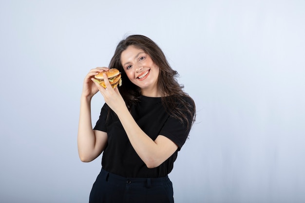 Hermosa joven sosteniendo una deliciosa hamburguesa de ternera.