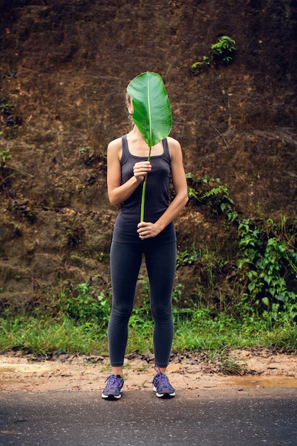 Hermosa joven sosteniendo una enorme hoja de una planta tropical