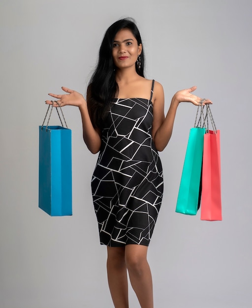 Hermosa joven sosteniendo y posando con bolsas de la compra en un gris