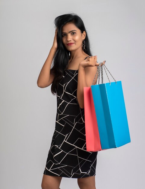 Hermosa joven sosteniendo y posando con bolsas de la compra en un gris