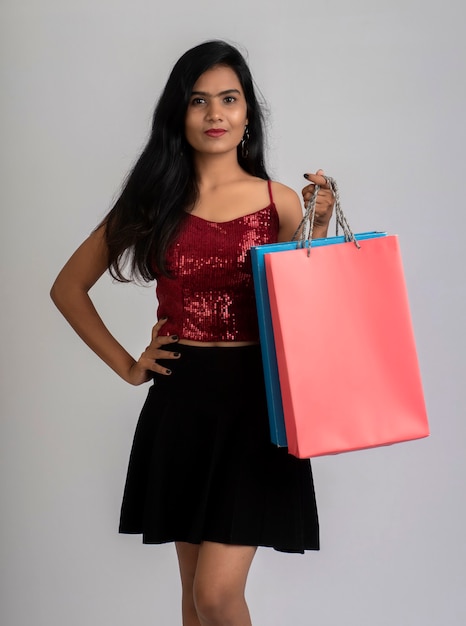 Hermosa joven sosteniendo y posando con bolsas de la compra en un gris