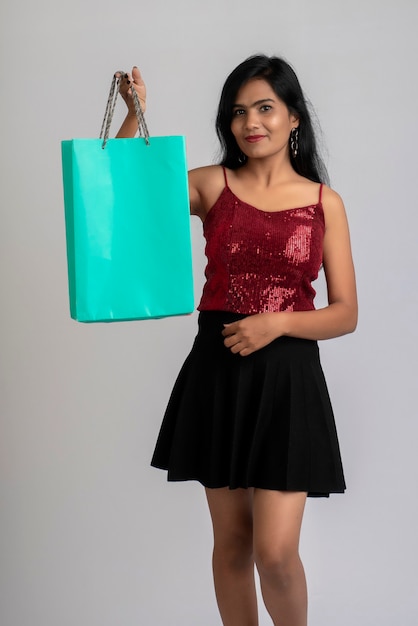 Hermosa joven sosteniendo y posando con bolsas de la compra en una pared gris