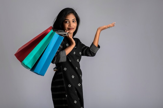 Hermosa joven sosteniendo y posando con bolsas de compras en un gris