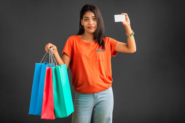 Hermosa joven sosteniendo y posando con bolsas de compras y tarjeta de crédito o débito en un fondo gris