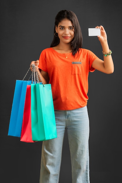 Hermosa joven sosteniendo y posando con bolsas de compras y tarjeta de crédito o débito en un fondo gris