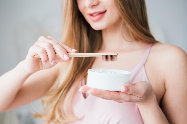 Hermosa joven sosteniendo un útil cepillo de dientes de bambú y un frasco de polvo dental. El concepto de un estilo de vida saludable, respeto por el medio ambiente y cero desperdicio. Viraje.