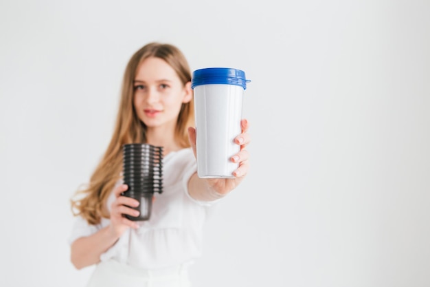 Hermosa joven sosteniendo un vaso reutilizable útil y vasos de plástico desechables para comparar. El concepto de sostenibilidad y cero residuos. Viraje. Enfoque selectivo.