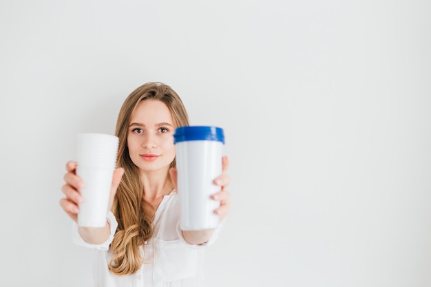 Hermosa joven sosteniendo un vaso reutilizable útil y vasos de plástico desechables para comparar. El concepto de sostenibilidad y cero residuos. Viraje. Enfoque selectivo.